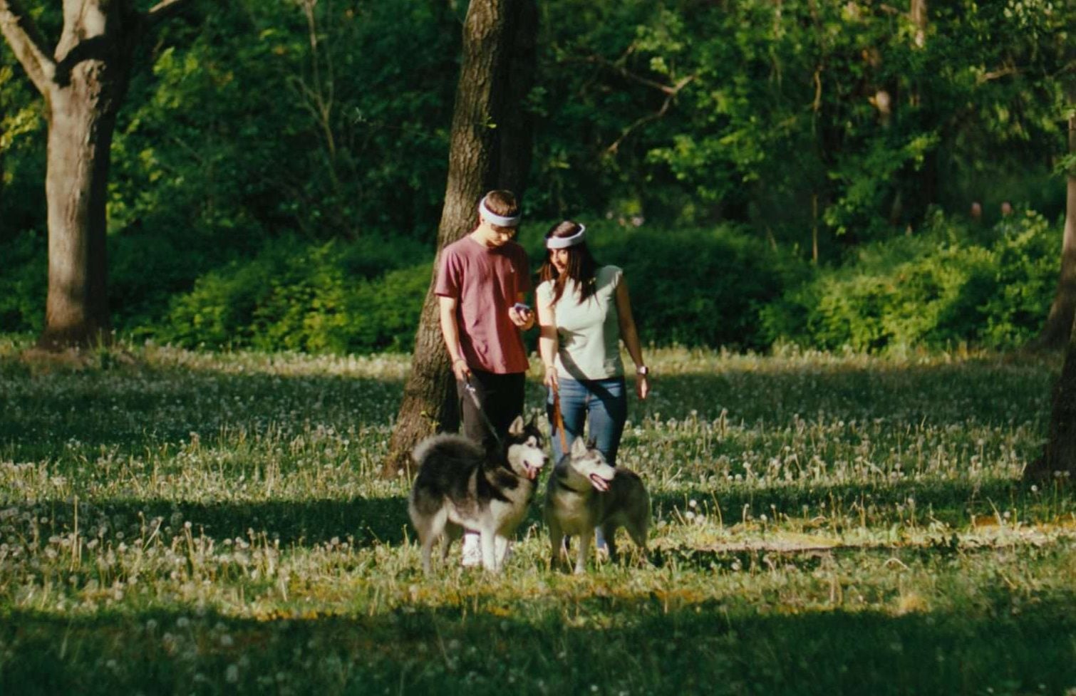 Image shows two people walking dogs in the woods. Both people are wearing Rezon Halos® brain protection.